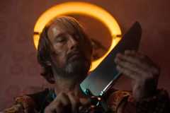 Image from Dust Bunny by director Bryan Fuller. It shows Mads Mikkelsen, a surgeon's blade in hand, examining the blade. A yellow halo sits over his head.